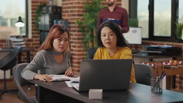 Asian Women Looking at Laptop Screen to Research Finance alt
