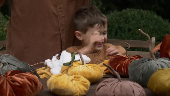 mother with son make pumpkins made of fabric on wooden table in garden alt
