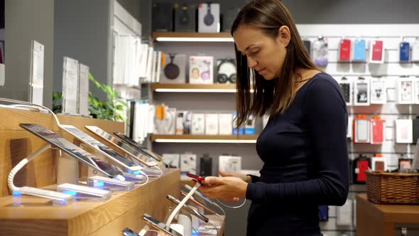Young Woman Chooses a New Smartphone in an Electronics Store.