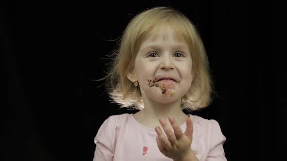 Child with Dirty Face From Melted Chocolate and Whipped Cream Eats Strawberry alt