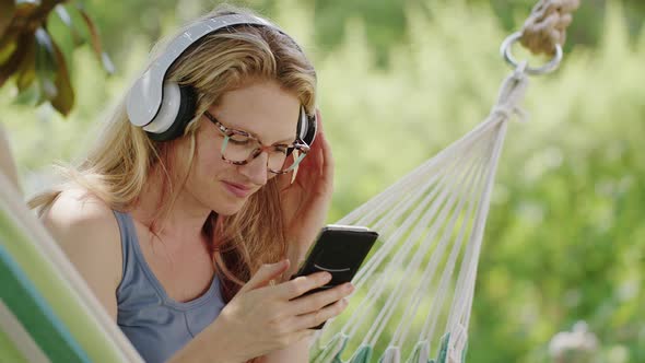 Smiling blonde woman wearing glasses using smartphone, listening to music