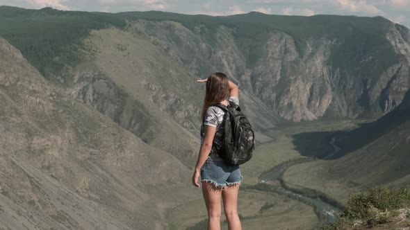 Female Traveler with a Rucksack Stands on Top of a Mountain and Looks Ahead alt