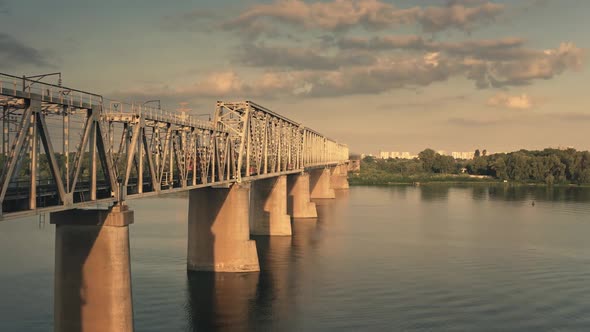 Aerial Sunset Train Crossing River By Railway Bridge