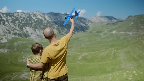 Father with his son play together with a toy blue plane on a background of mountains in Montenegro alt