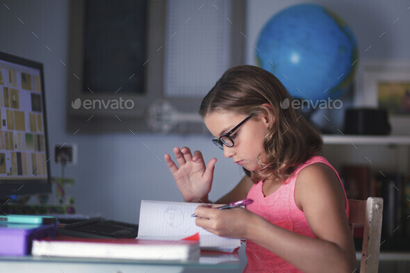 Young girl sitting at desk, doing homework, looking through book Stock ...