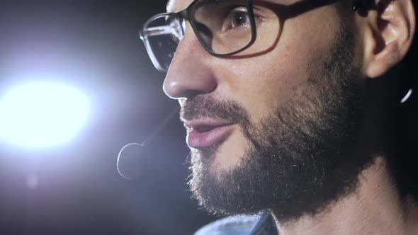 Portrait of a Young Male Business Coach Speaking Through a Microphone in a Dark Conference Room alt