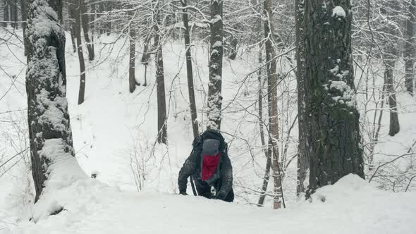Man with a Tourist Backpack Climbs a Snow Covered Hill