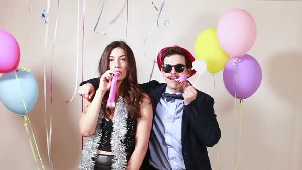 Beautiful couple blowing party horns in photo booth alt