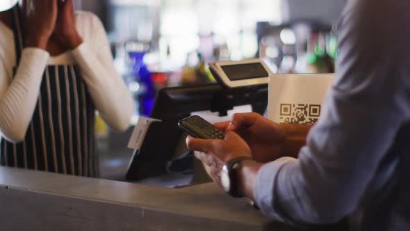 Mixed race man giving african american female cafe worker his credit card in order to pay alt