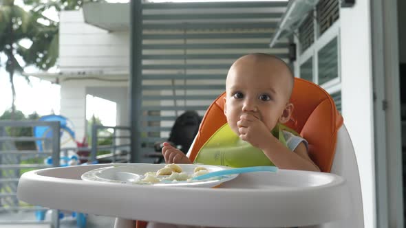 Cute Baby Boy Sitting on High Chair Eating Food By Himself
