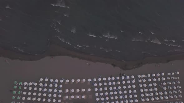 Aerial View of Sandy Beach with Sunbeds and Wooden Umbrellas at Sunset