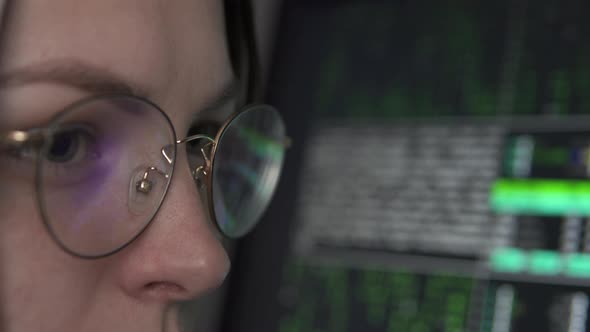 A female hacker works at a computer at night in the dark. alt
