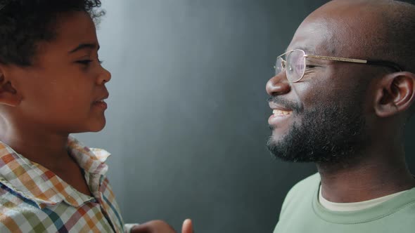 Portrait of Smiling Afro Father and Little Son against Black Wall alt