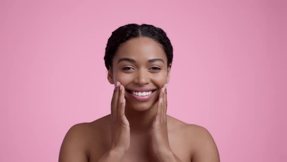 Young Beautiful Black Woman Rubbing Moisturizing Cream Dots on Her Cheeks Smiling to Camera with alt