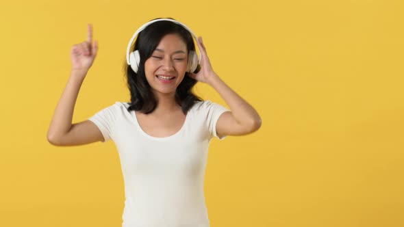 Young happy smiling Asian woman in white t-shirt listening to music on headphones and dancing