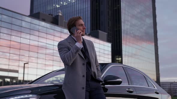 Cityscape Portrait of a Young Businessman Standing Near a Business Car and Talking on a Mobile Phone alt