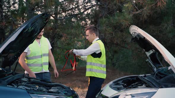 Two Men in a Green Safety Vest are Talking to Each Other Recharging Battery on the Road alt