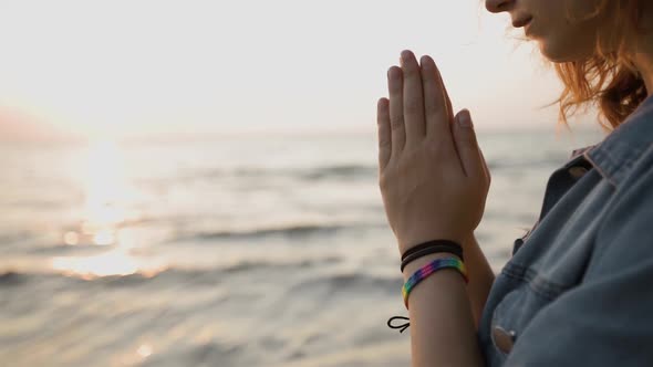 LGBT Pride: Hands Close View of Young Woman Wearing Rainbow Bracelet and Praying at Sea alt