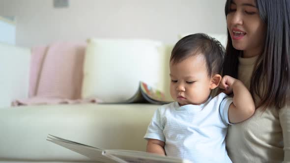 Young mother and little boy child reading book sitting on floor near sofa at home. Happy family.