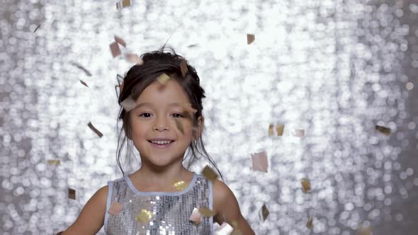 Cute Happy Little Girl Child in a Silver Dress Dancing on Background of Silver Bokeh