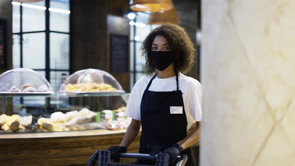 African American Female Worker Pushing Trolley in Supermarket Wearing Protection Mask alt