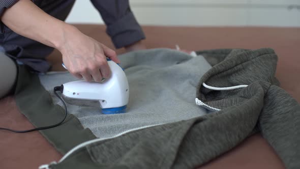 Woman Uses a Machine for Removing Pellet and Spools From Clothes and Fabric on Black Trousers