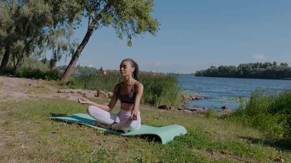 Young African Woman in Lotus Yoga Position Sitting Outdoors Near the River alt