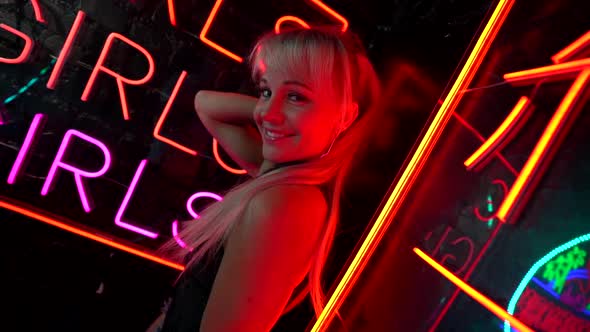 Joyful Go-go Dancer Woman Is Flirting with Camera, Portrait Against Signboard of Nightclub with Neon alt