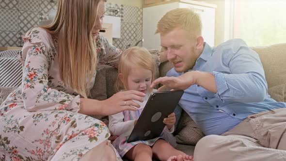 Cheerful Caucasian Family with Little Girl Sitting on the Sofa, Laughing While Watching Something alt