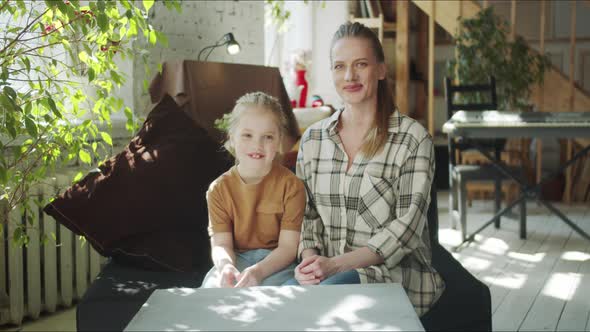 Young Mother and Daughter are Sitting on the Sofa in a Large Apartment alt