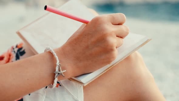 Close up view of a woman writing in her diary at sunset sitting on beach