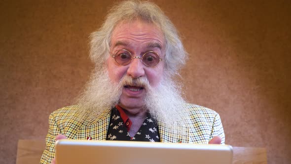 Older man with beard suprised from talking to someone over device alt