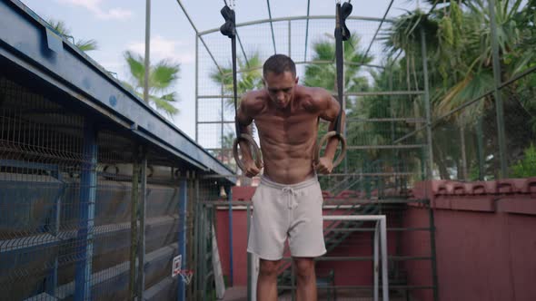 Muscular Athletic Young Man Exercising on Gymnastic Rings alt