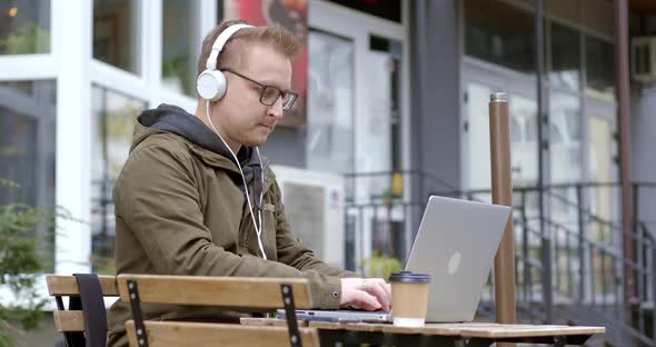 Business man in headphones works online using a laptop while sitting in a cafe on the street.  alt