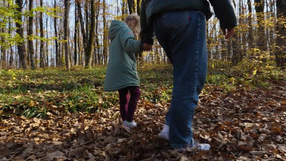 In slow motion, mother and daughter holding hands are walking through an autumn forest alt