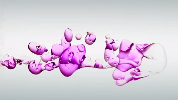 Oddly Satisfying slow-motion floating vivid purple oil against off white background in clear water. alt