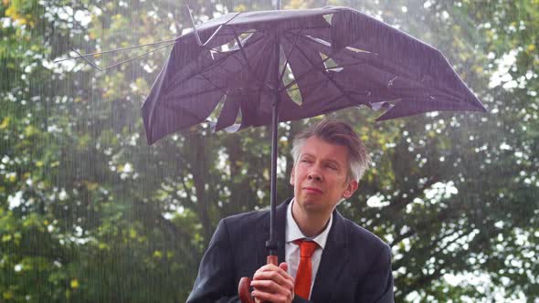 Businessman Sheltering Underneath a Broken Umbrella in the Rain