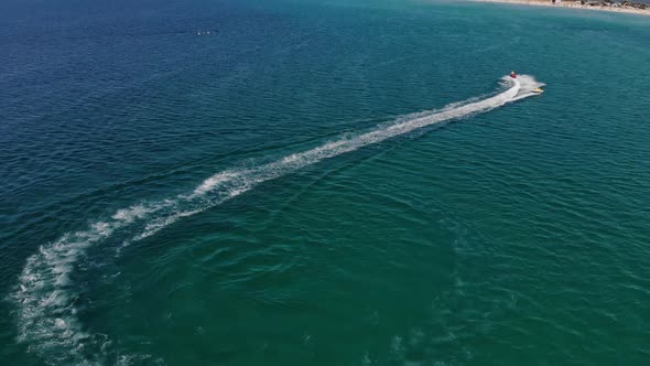 Aerial View of Inflatable Towed Tubes to Roll Tourists on a Tube Tied to Jetski Across the Azure Sea alt
