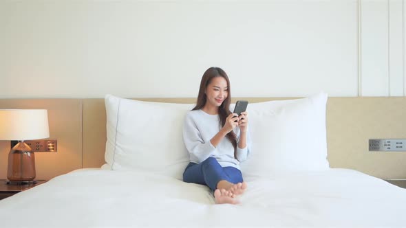 Young pretty asian woman texting on smartphone in bed, social networking concept full frame alt