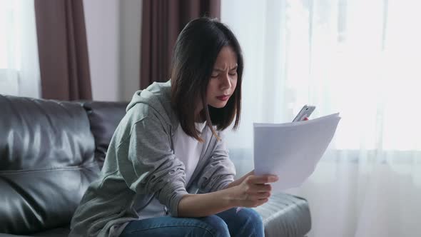 Woman holding the bill and smartphone in the living room and stressed by excessive expenses alt
