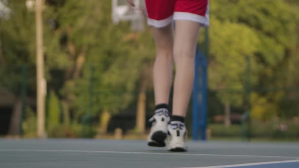 The Basketball Ball Lies on the Sports Ground. Unrecognizable Player Picks Up the Ball and Dribbling alt
