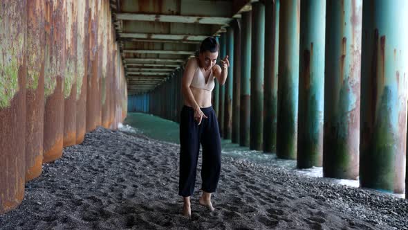 a Woman Dances Under the Pillars of the Bridge Against the Background of the Incoming Waves alt