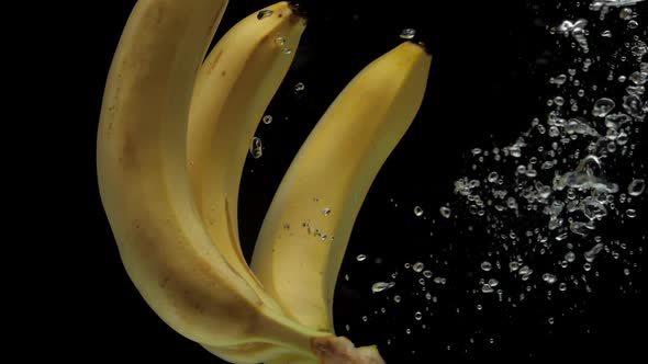 Slow Motion Bananas Falling Into Transparent Water on Black Background alt