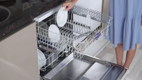A Woman's Hand Puts Dirty Plates and Mugs on the Top Shelf of the Dishwasher