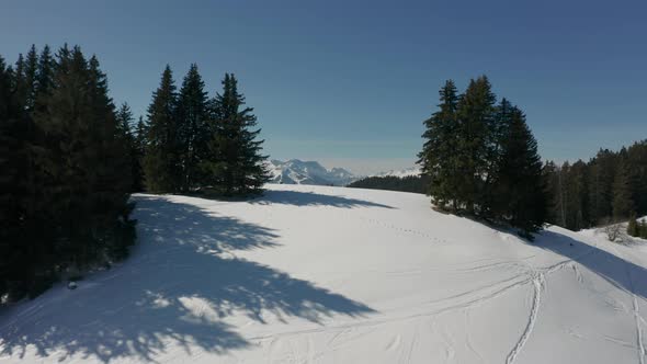 Drone flying over snow covered hill and revealing a stunning valley with green forest alt