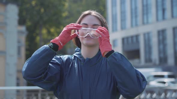 Joyful Brunette Woman Taking Off Respirator and Eyeglasses and Unzipping Chemical Suit. Portrait of alt