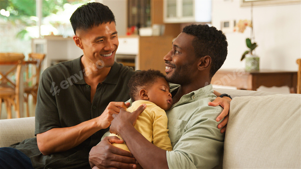 Same Sex Male Couple Smiling While Holding a Sleeping Child in a  