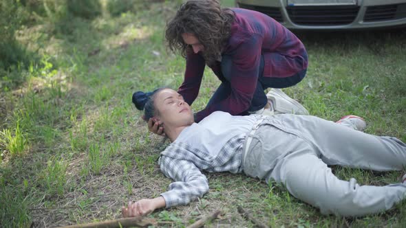 Unconscious Knocked Down Woman Lying on Ground with Man Raising Head Checking Pulse alt