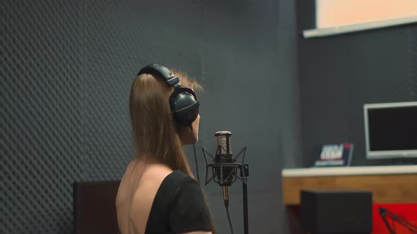 Positive Woman in Dress with Open Back Sings to Microphone alt