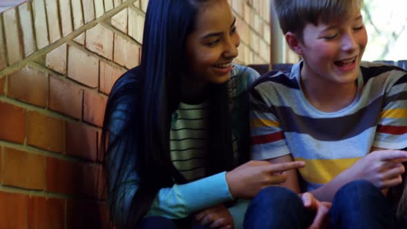 Smiling school students sitting on the staircase using mobile phone alt